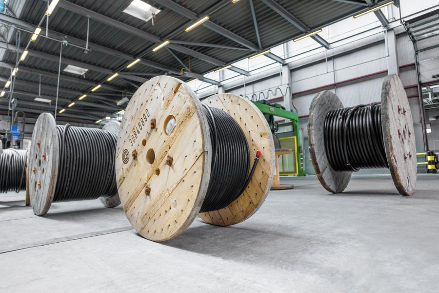 Große Kabelspulen mit schwarzem Draht in einem Lager, festgehalten in professioneller Industriefotografie.